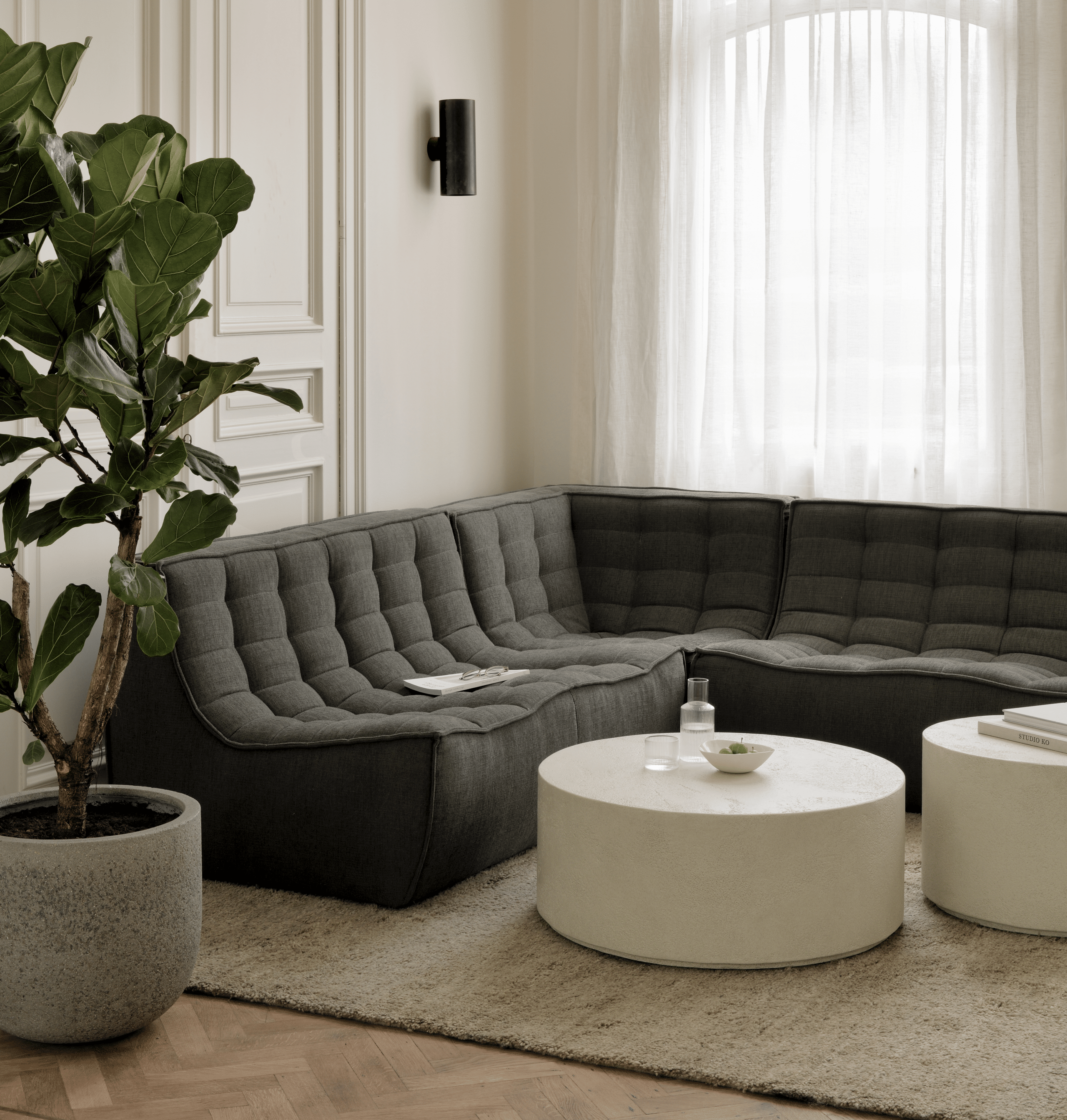 Living room furnished with Ethnicraft furniture from Belgium. The modular sofa comprises a two-seater, a three-seater, and a corner seat. The sectional is upholstered in sustainable Moss green Eco fabric in recycled cotton. The seats are armless, button-tufted, and fitted with scoop seats. Designed by Jacques Deneef for longevity and ultimate comfort for any body type. The seating is shown with two sturdy microcement creamy white round coffee tables from Ethnicraft's Elements collection. Order Ehnicraft furniture pieces from the N701 and Elements collections at D3 Home Modern Furniture in San Diego.