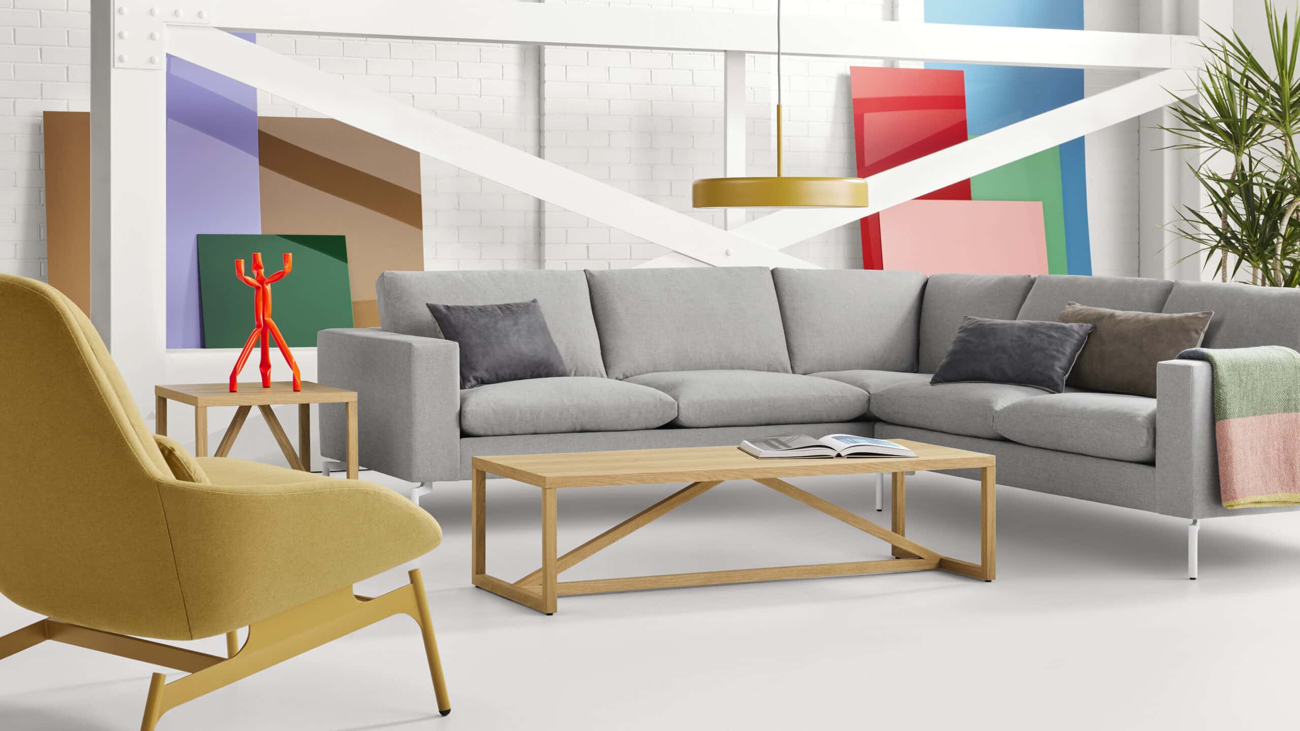 The living room is furnished with a Blu Dot New Standard Sectional sofa with white legs and is upholstered in Spitzer Grey fabric. The sectional is L-shaped, with arms, seat, and back cushions. To the left of the sofa is the Blu Dot Field Lounge Chair upholstered in Maharam Candor in Flare fabric, a muted mustard-yellow color. The white oak coffee and side table are from Blu Dot's Strut series. Overhead hangs the round Bobber Large Pendant Light in Mustard. Blu Dot Furniture is available at D3 Home Modern Furniture in San Diego.